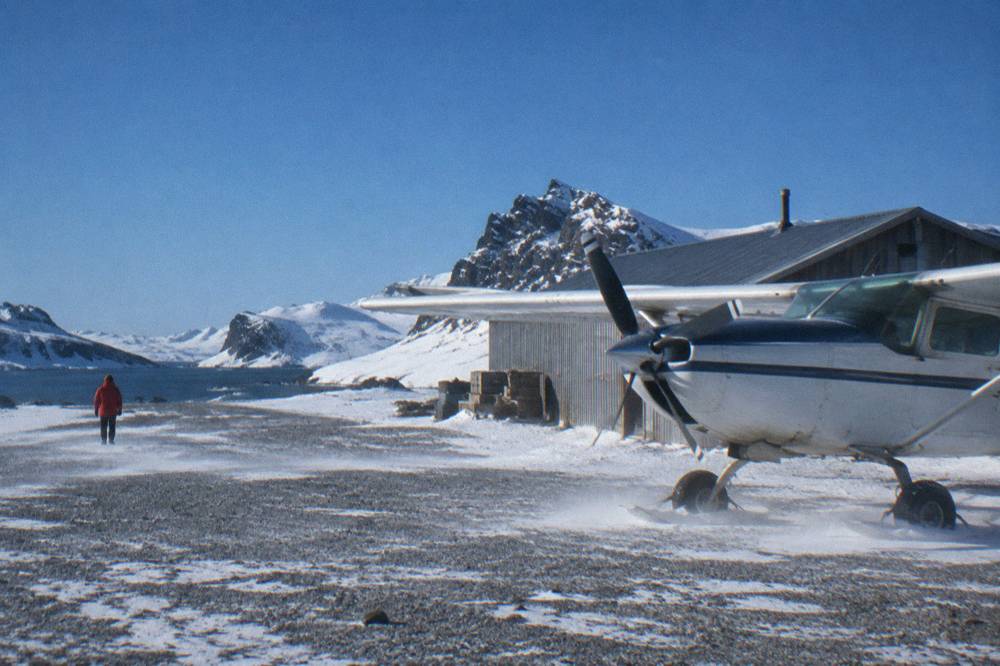 A small aircraft on a gravel airstrip beside a shelter on a snowy sub-Antarctic island