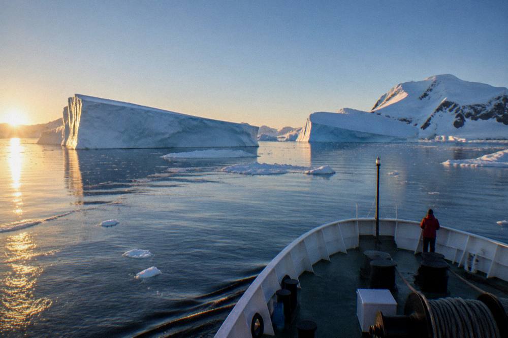 A luxury expedition ship's bow cutting through calm polar water at low golden light