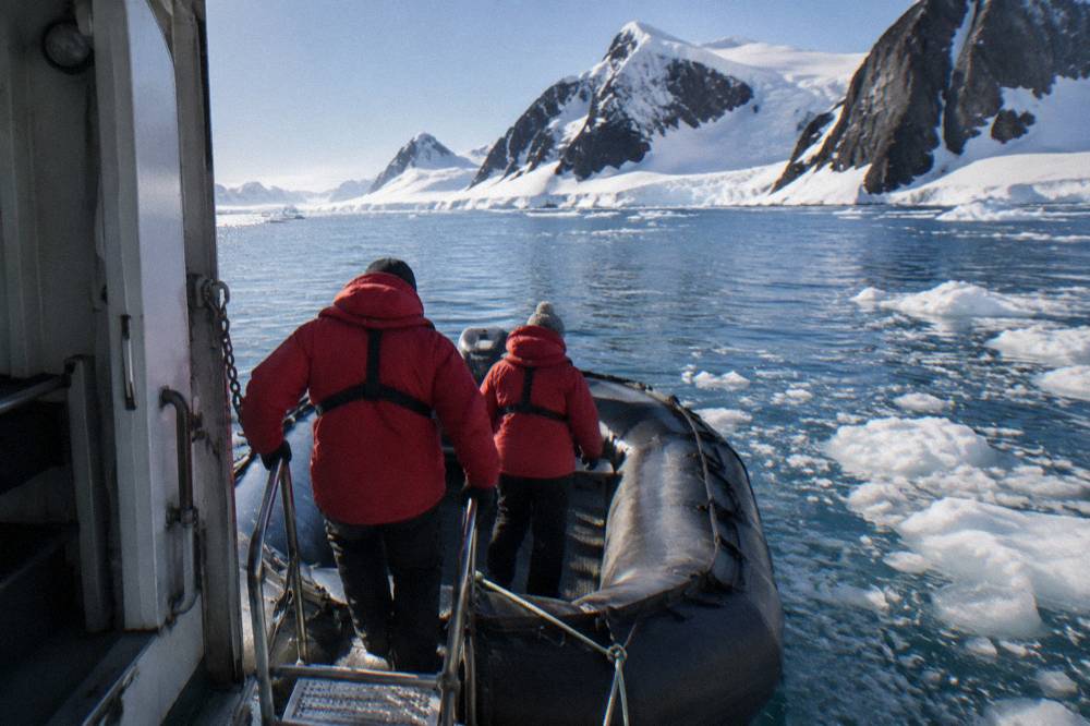Guests in red parkas boarding a Zodiac beside an expedition ship in Antarctica
