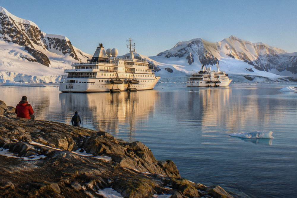 Two expedition ships at anchor in a calm Antarctic bay ringed by glaciers