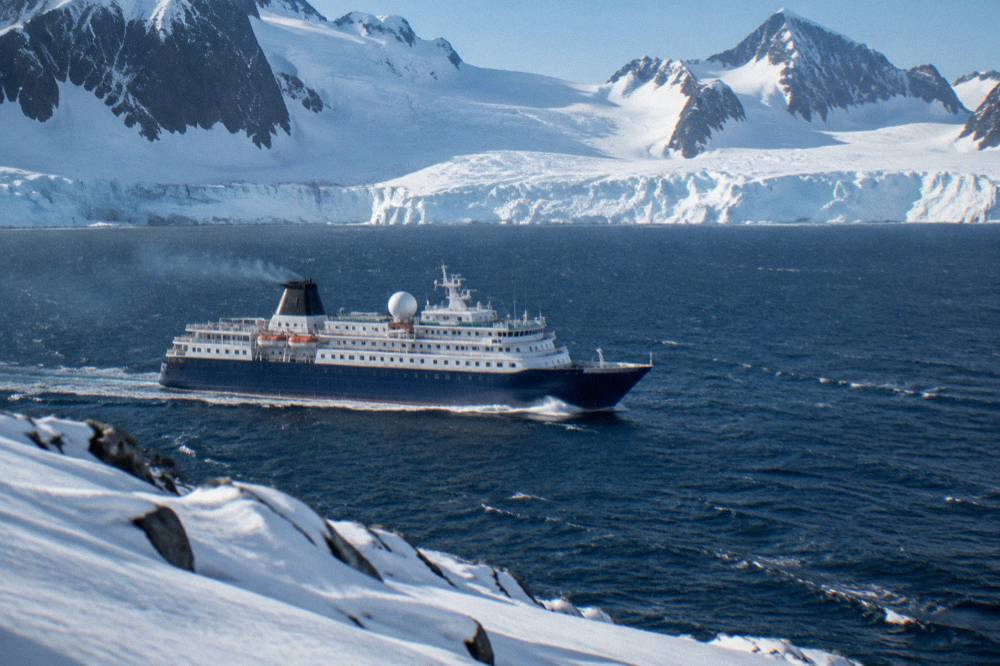 An expedition ship sailing past snow-covered mountains along the Antarctic Peninsula