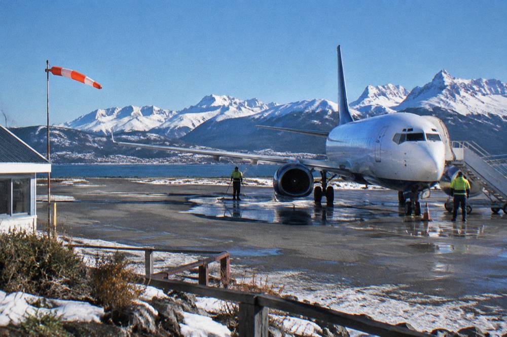 A commercial jet parked on a small runway ringed by mountains at the edge of a town