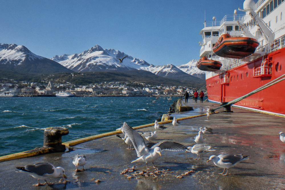 A red-hulled expedition ship with small boats on its side davits moored at a quay