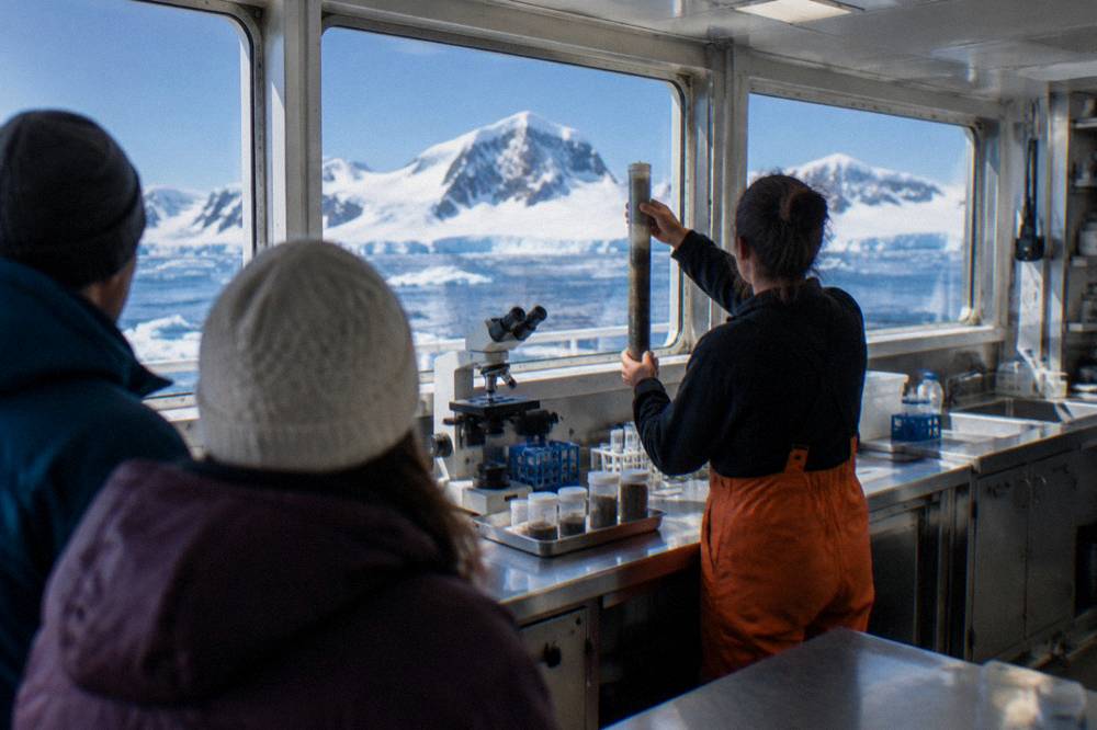 A shipboard laboratory interior with scientific instruments and a staff member showing guests a sample.
