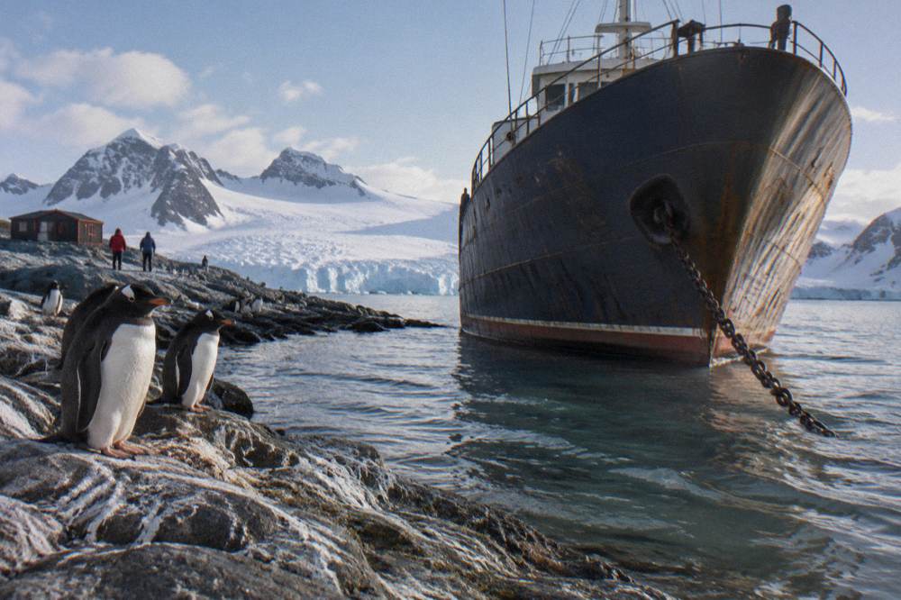 Small expedition ship at anchor in a sheltered Antarctic cove with snowy peaks behind