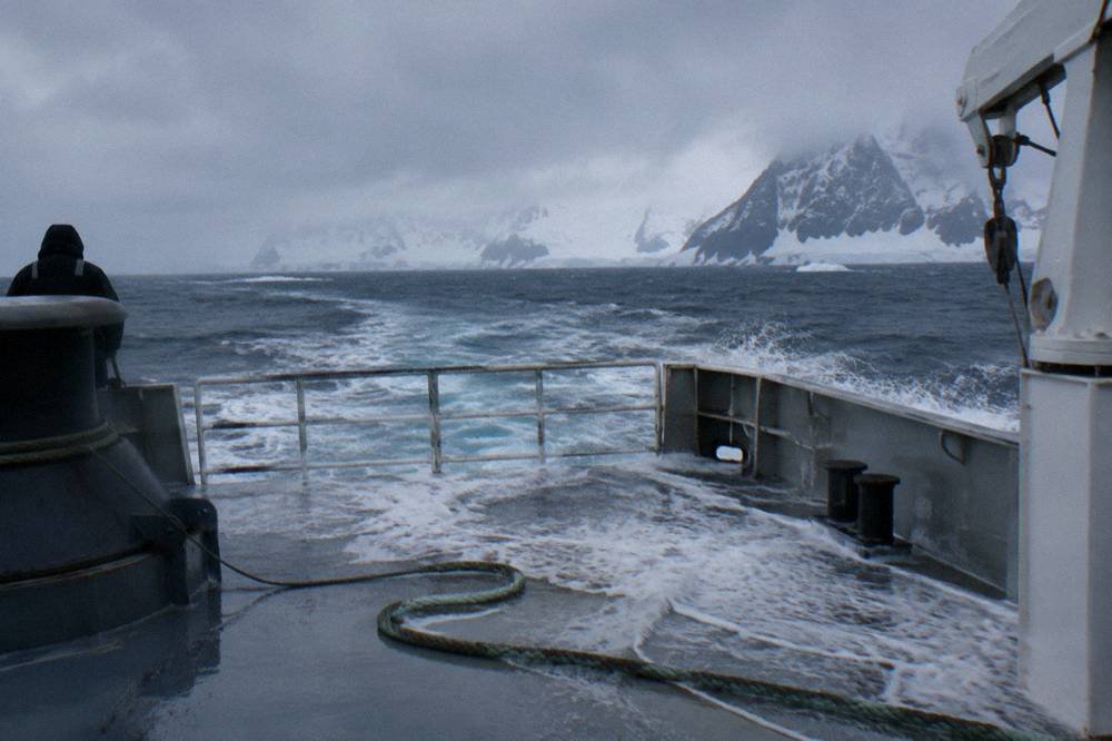 An expedition ship seen from astern plowing through grey open ocean swell