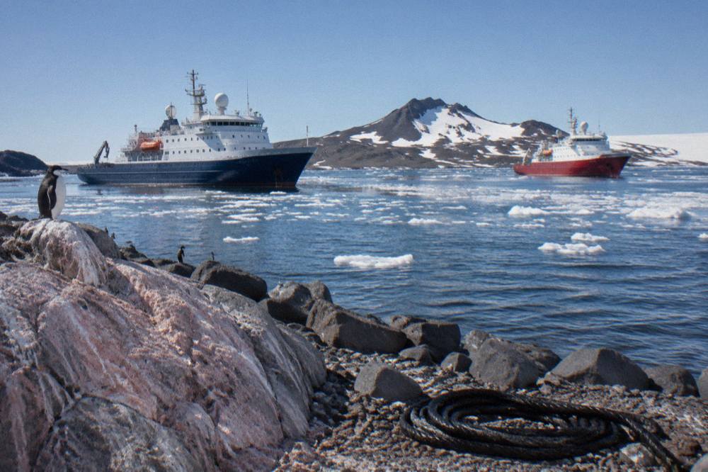 Two expedition ships at anchor in a calm Antarctic bay surrounded by brash ice