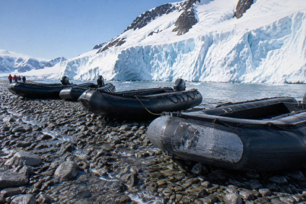 Zodiacs lined up on a rocky Antarctic beach below a glacier face