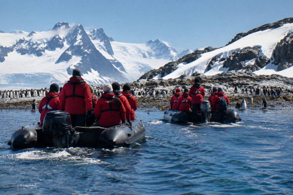 Zodiac boats carrying passengers toward a penguin colony on a rocky Antarctic beach