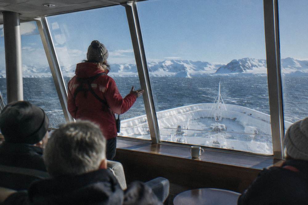 Expedition team member briefing passengers in a glass-walled observation lounge