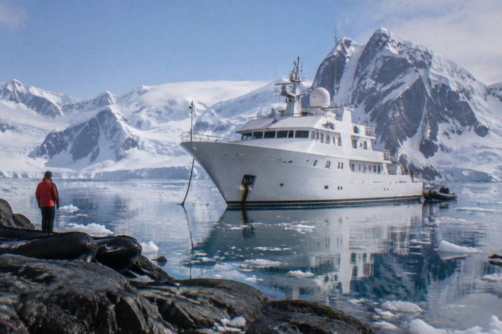 An expedition yacht anchored in a calm Antarctic bay with snow-covered mountains behind it