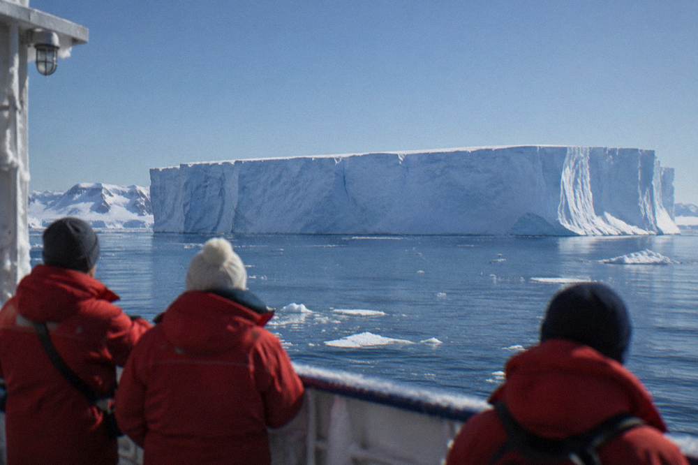 Passengers in red parkas watching icebergs from the open deck of a small ship